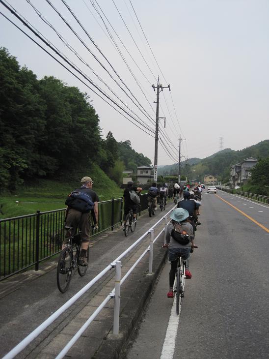Rear view of cyclists riding down a street and bike trail, with a rail between them, with buildings and hills ahead